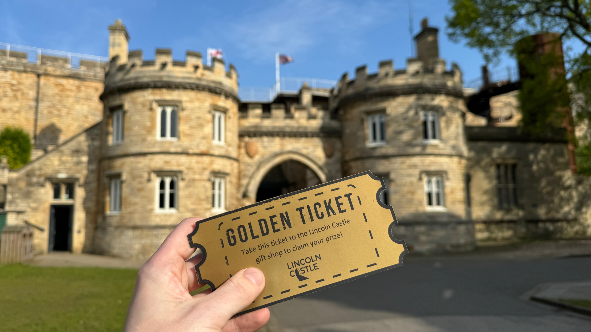 A golden ticket being held in front of the Eastgate at Lincoln Castle