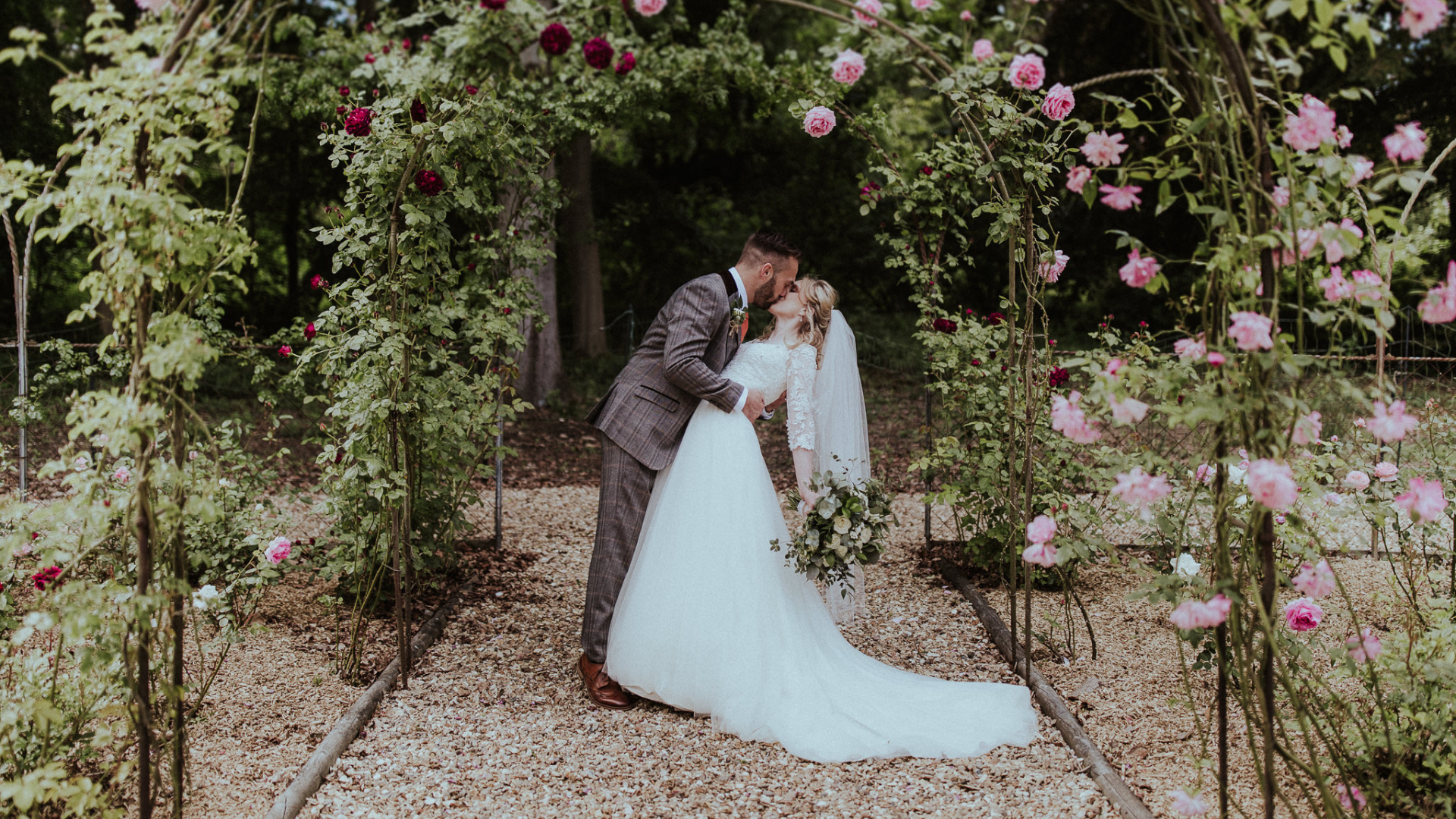 Bride and groom kissing under a rose arch in a garden