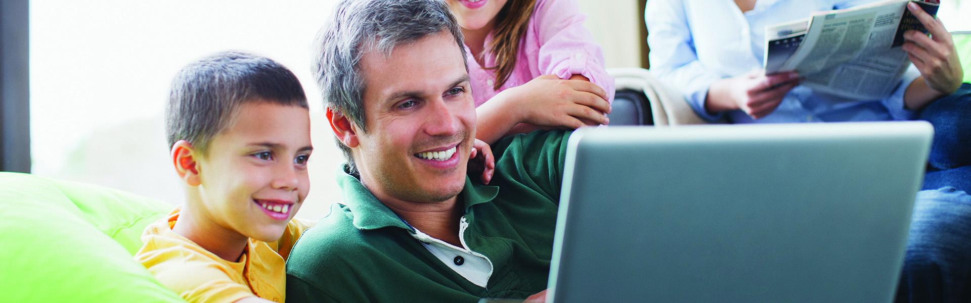 A man and a little boy and girl looking at a laptop, and smiling
