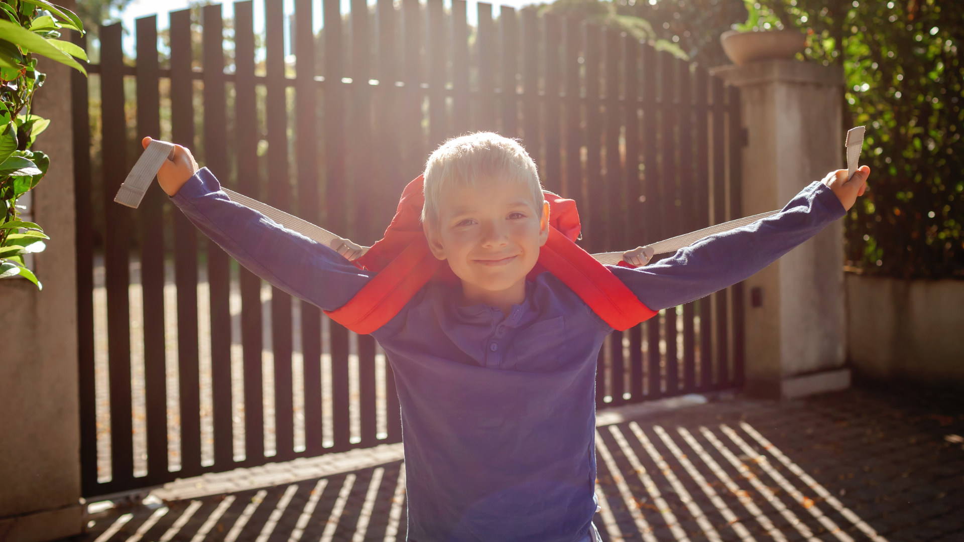 A young boy lifting his arms up holding his rucksack straps