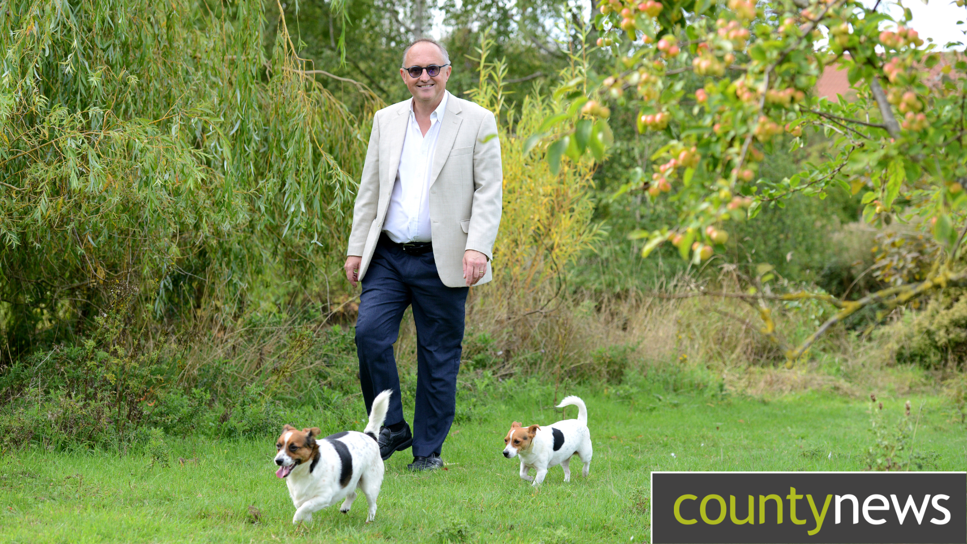 A man walking in the countryside with two white and tanned small terriers