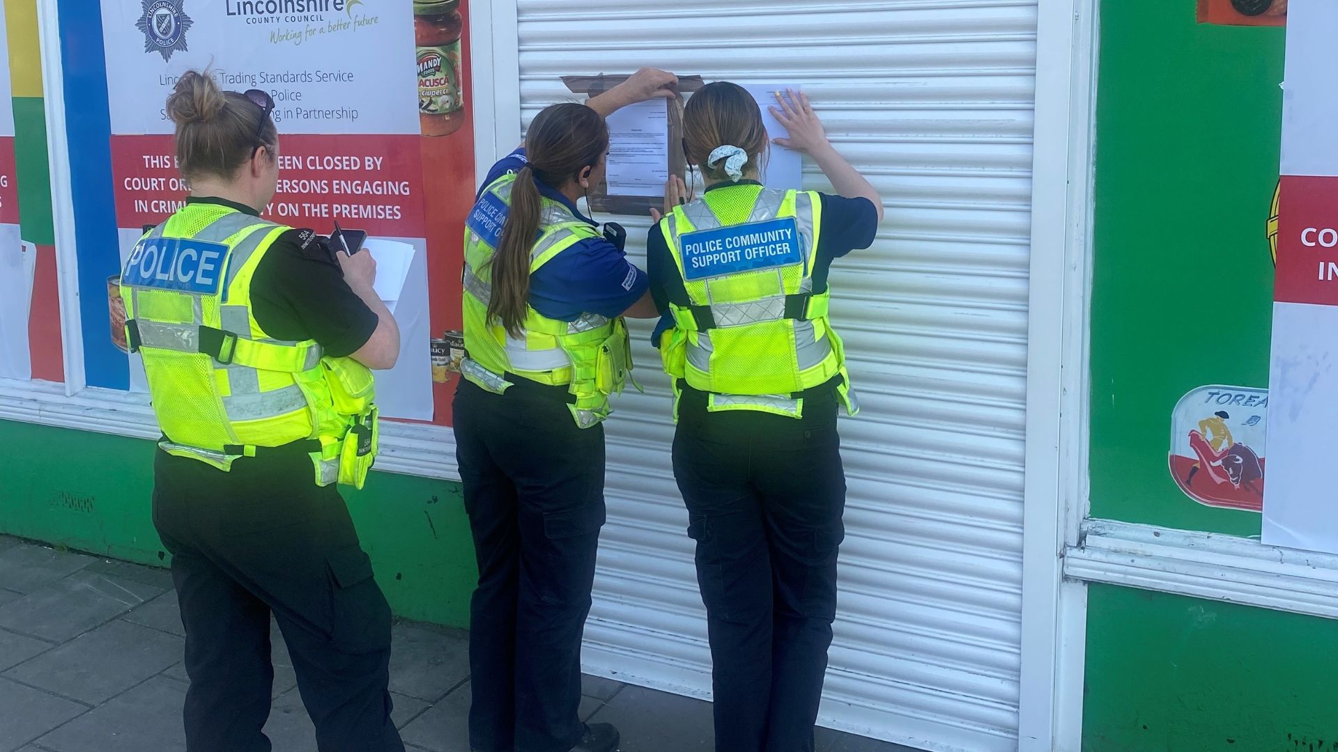 Police community officers shutting down a shop and adding enforcement notices to the window.