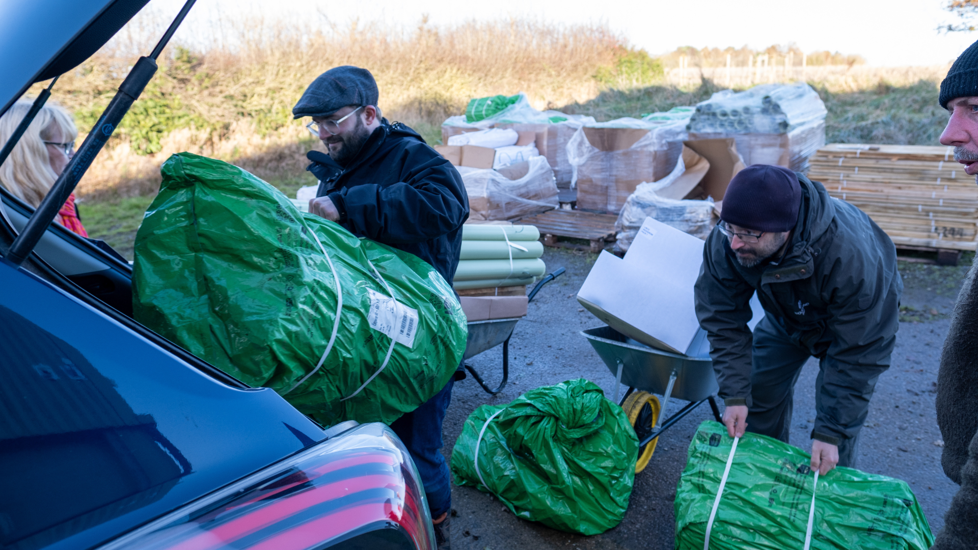 two men load tree planting materials into the back of someone's car