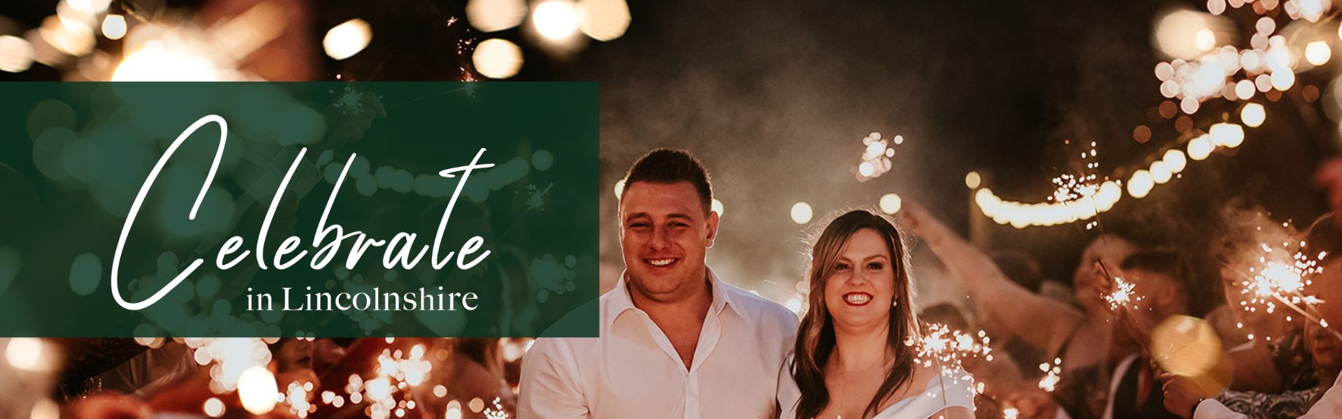 A wedding couple stood under the fairy lights holding sparklers in the dark.