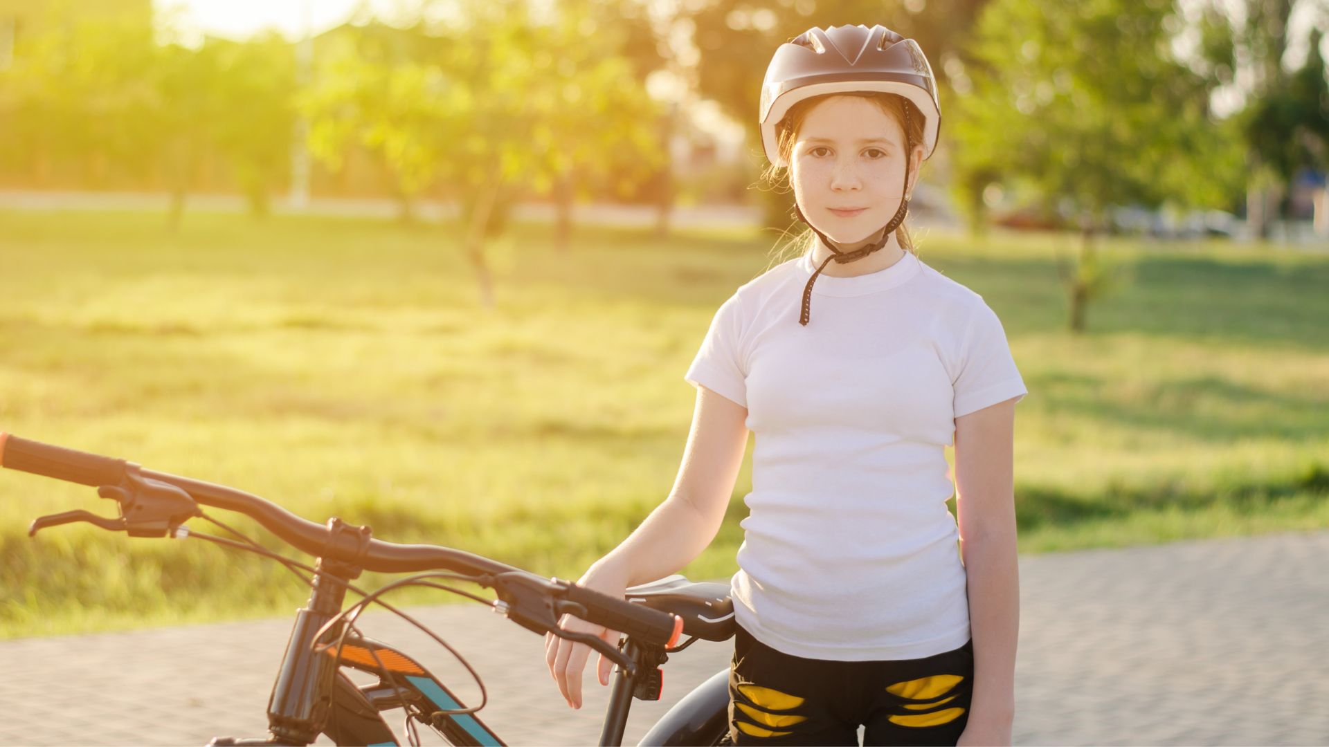 A young girl, stood holding a bike with a helmet on