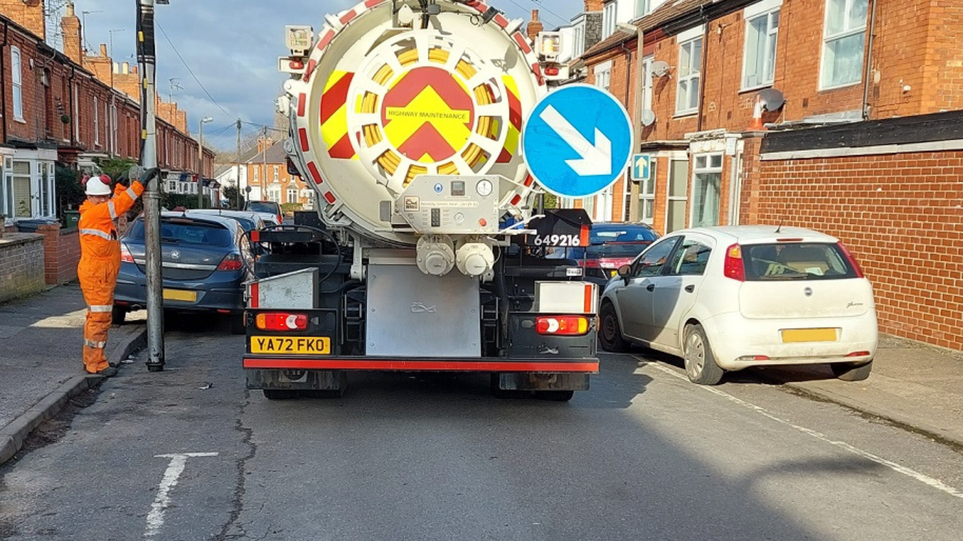 A Highways vehicle struggles to clear drains on a street lined with parked cars