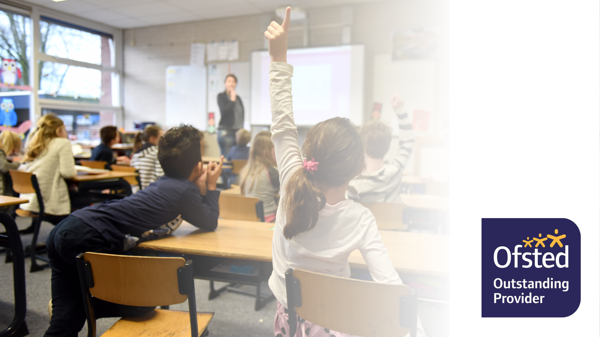 A classroom full of children sat down at desks putting their hands up