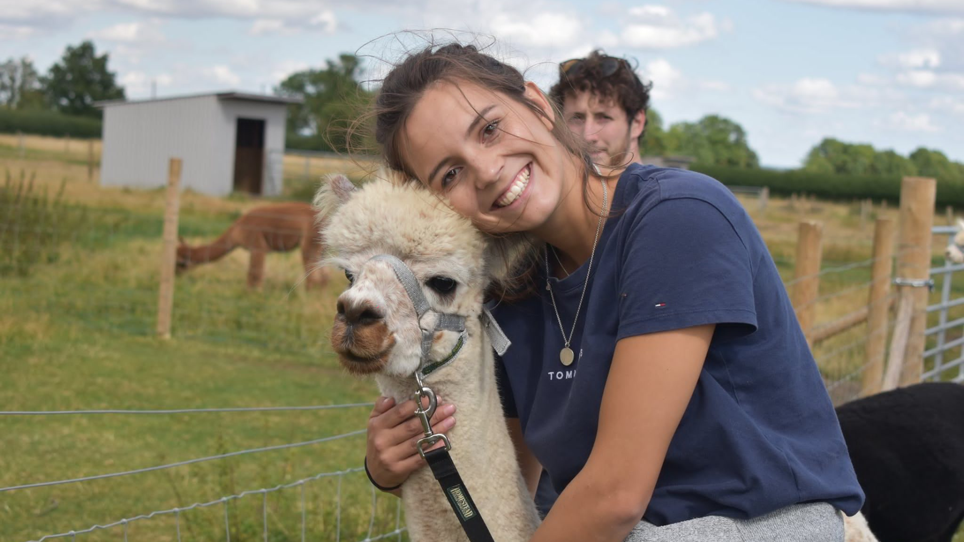 A lady smiles next to an alpaca