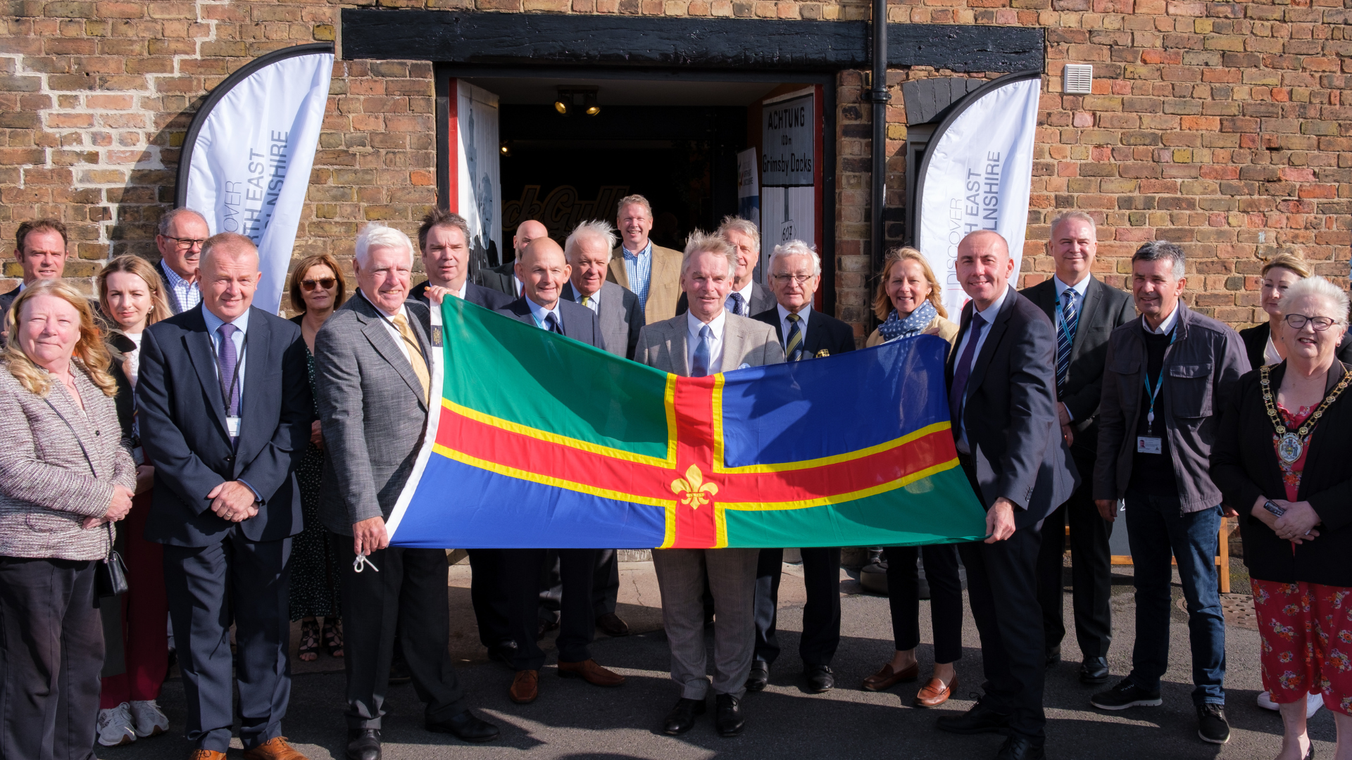 A crowd of people standing in front of a building holding the Lincolnshire Flag