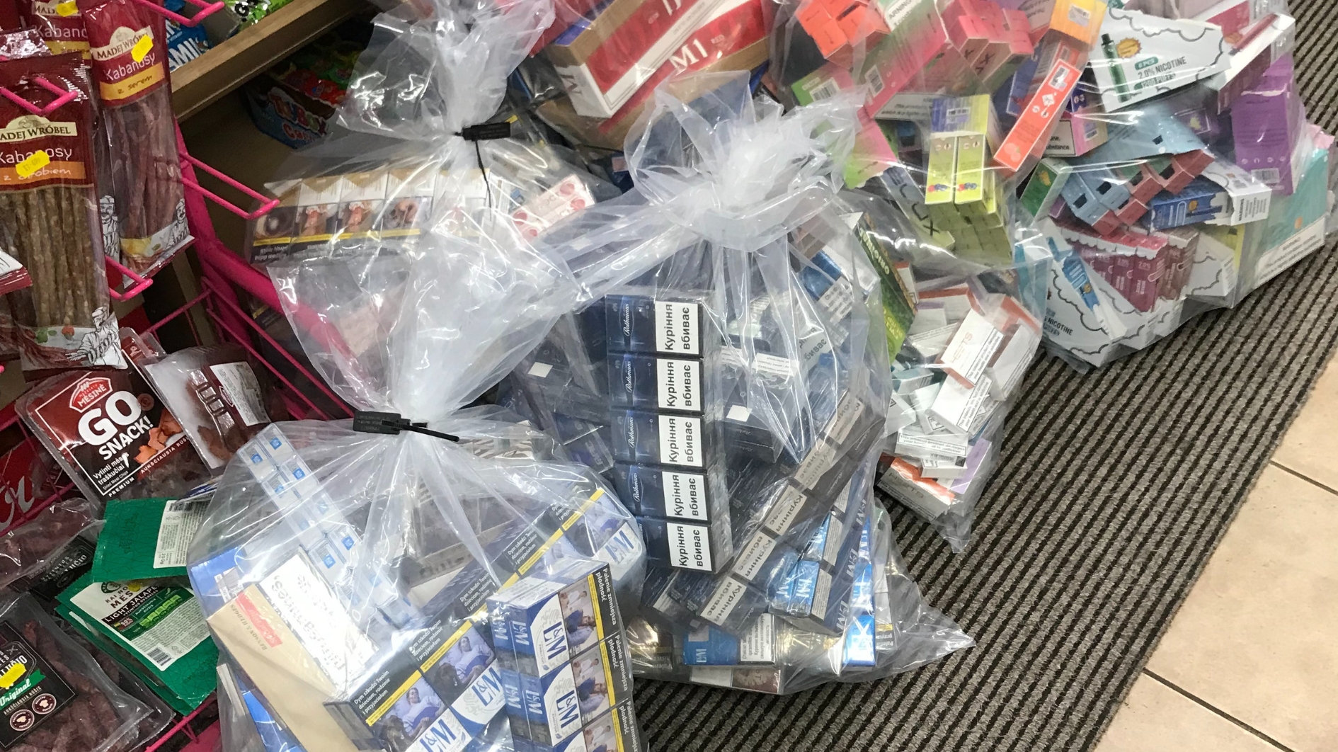 Bags of illegal cigarettes and vapes piled on a floor in a shop