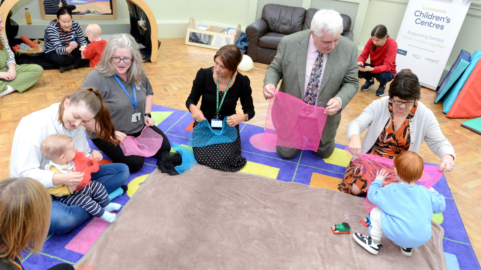 Adults doing activities with young children on their knees on the floor at a Children&#039;s Centre