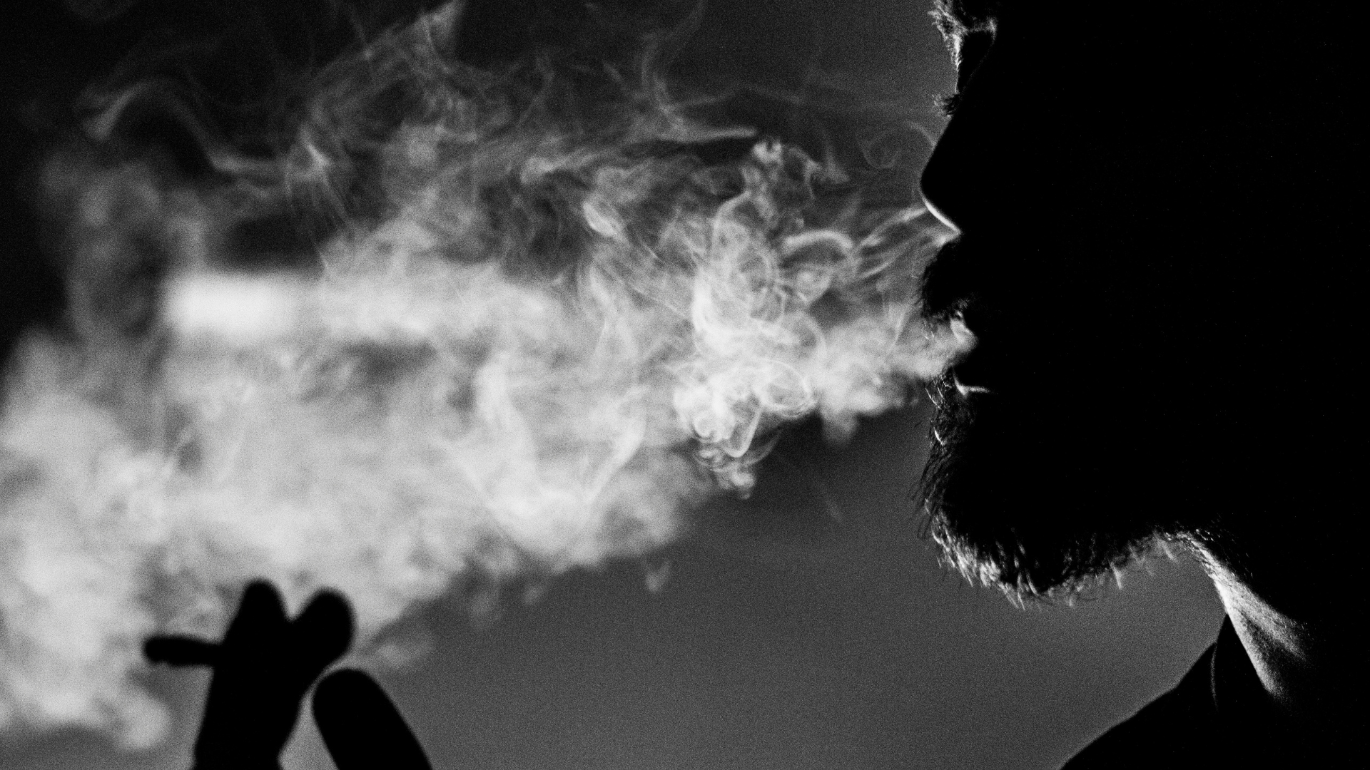 Silhouette of someone smoking and exhaling smoke.