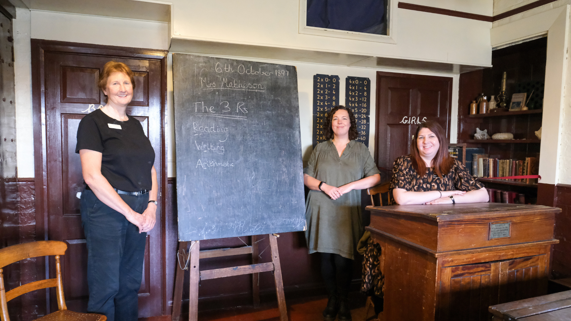 Three ladies stand around a Victorian style blackboard