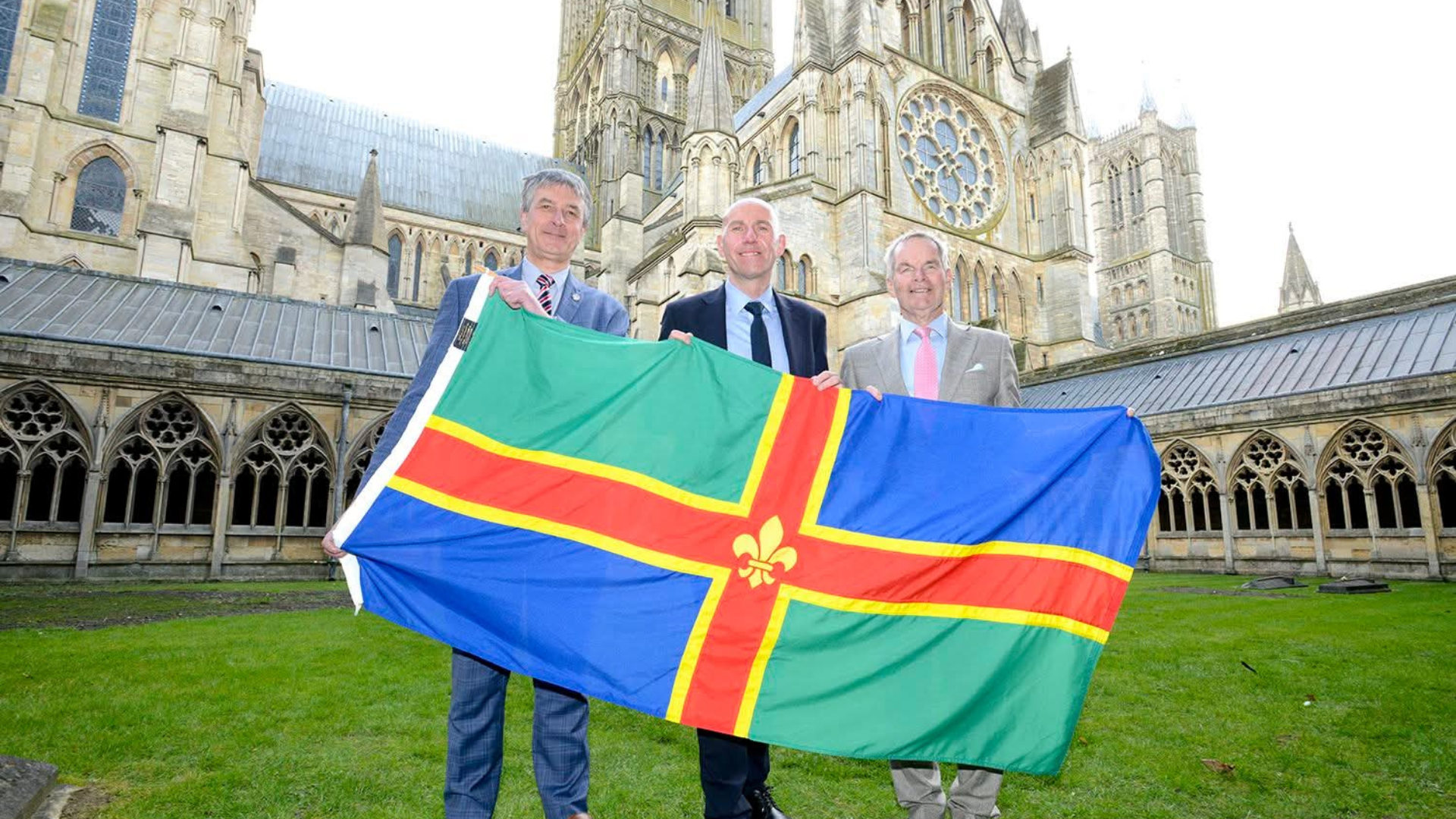 Three leaders at Lincoln Cathedral holding a Lincolnshire flag