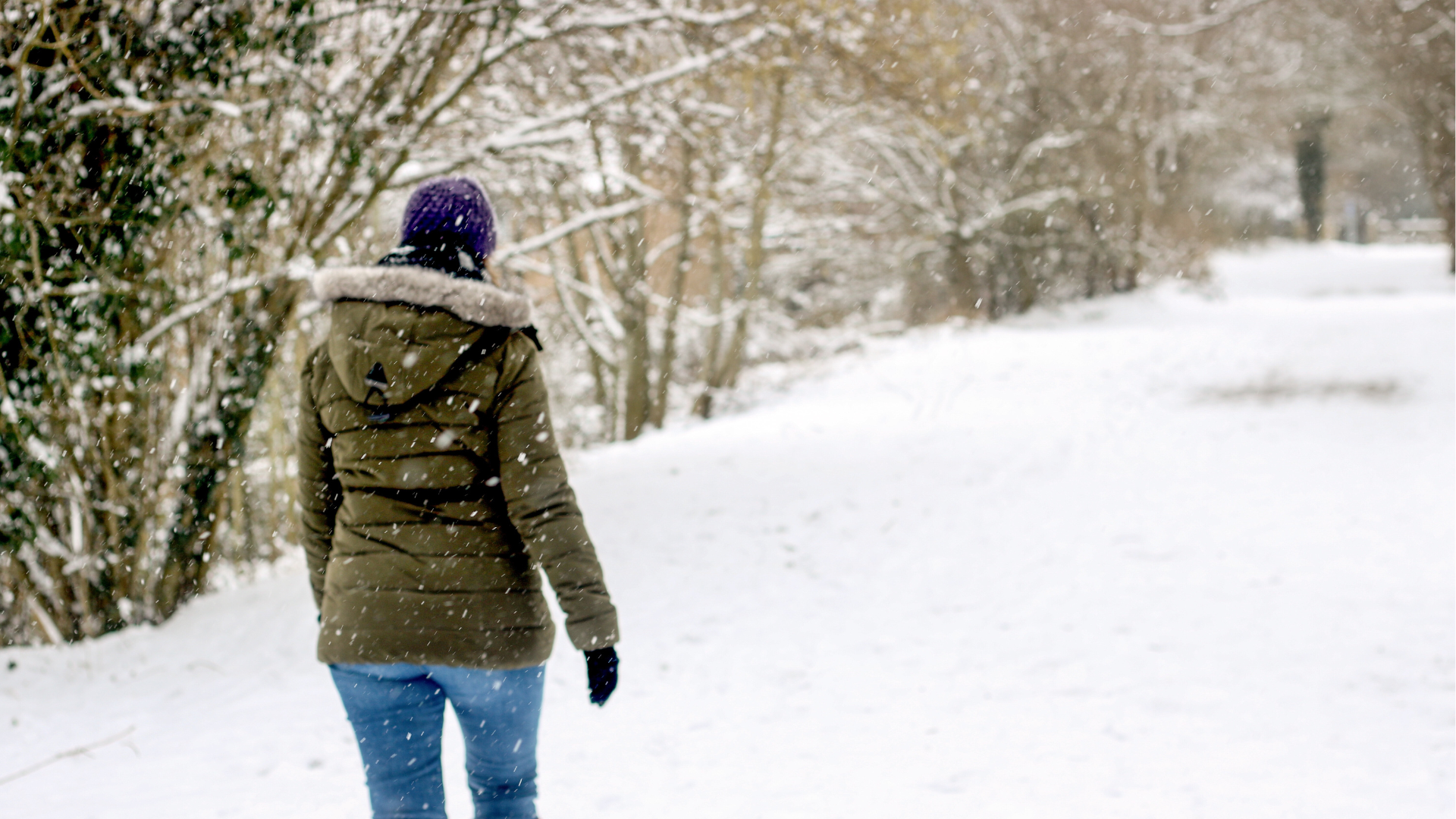 A woman walking away from the camera in the snow in the countryside