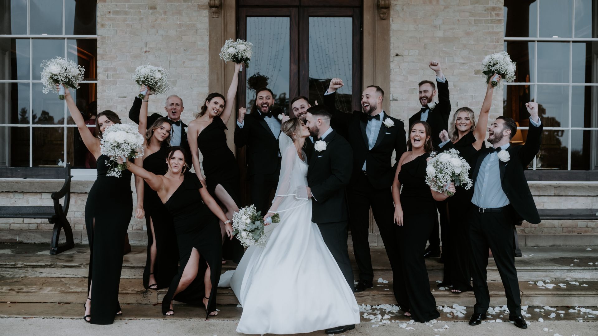 Wedding party stood around the bride and groom with bouquets and hands in the air