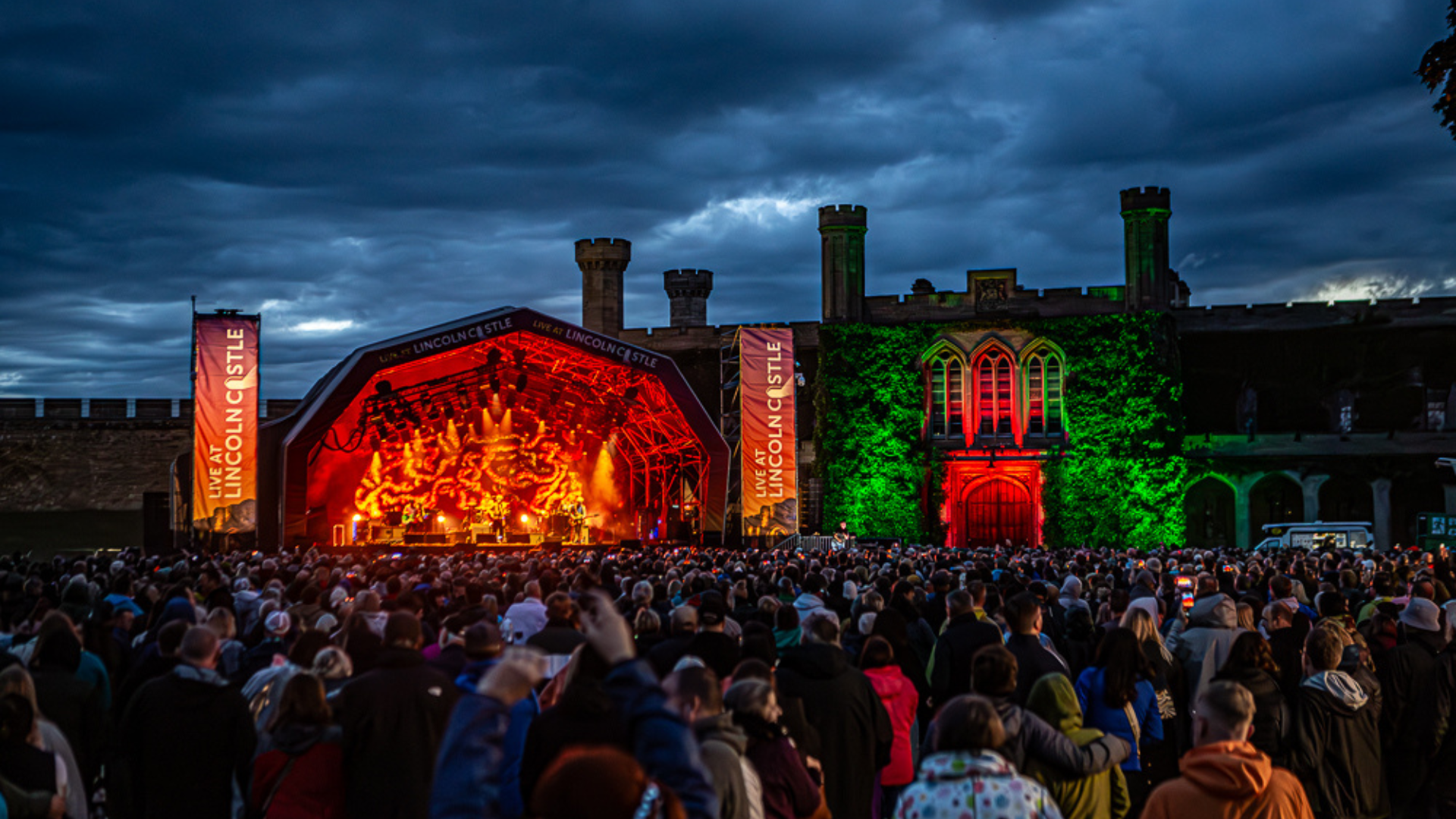 Stage in Lincoln Castle lit up at night with large crowd in front