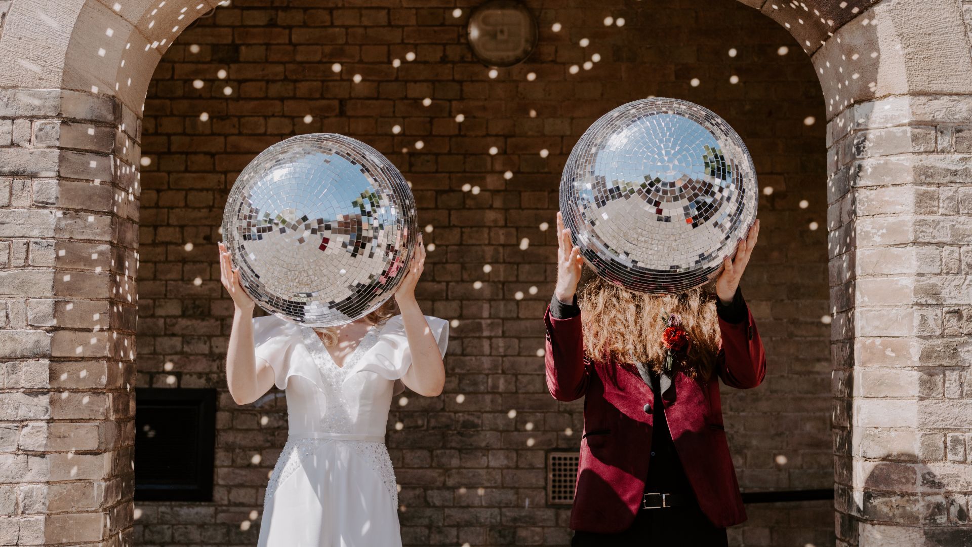 A bride and groom holding disco balls up to cover their faces